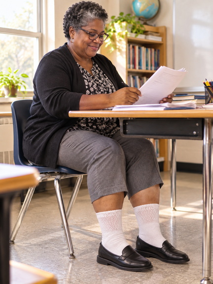 Teacher seated in a classroom, wearing wide-calf Diabetic Sock Club socks